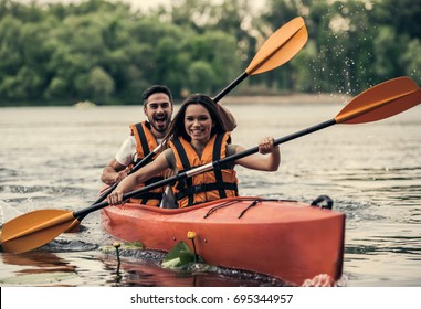 Happy Young Couple In Sea Vests Is Smiling While Sailing A Kayak