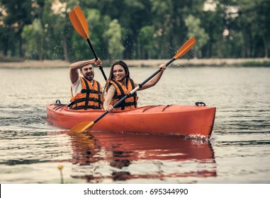 Happy Young Couple In Sea Vests Is Smiling While Sailing A Kayak