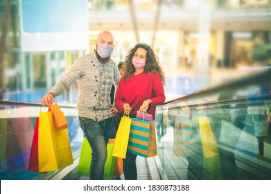 Happy young couple with shopping bags going up by escalator in mall - Boy and Girl with face mask make shopping - sale, consumerism and people new normal concept - Powered by Shutterstock