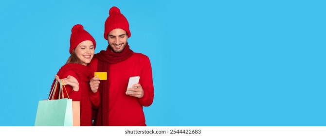 Happy Young Couple With Shopping Bags Using Smartphone And Credit Card, Cheerful Man And Woman In Winter Hats Using Mobile App For Online Purchases, Standing Over Blue Background, Copy Space - Powered by Shutterstock