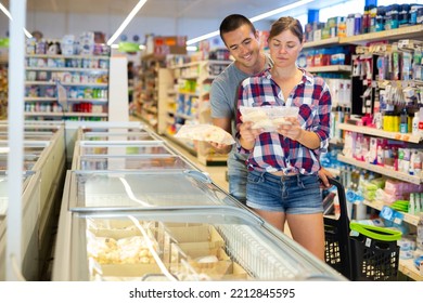 Happy Young Couple Shopping In Supermarket, Choosing Frozen Convenience Food For Quick Dinner..