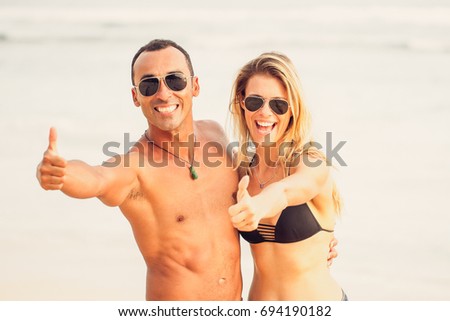 Happy young couple showing thumbs up on beach