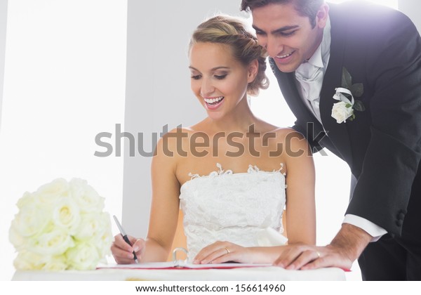Happy young couple signing wedding register sitting\
at desk