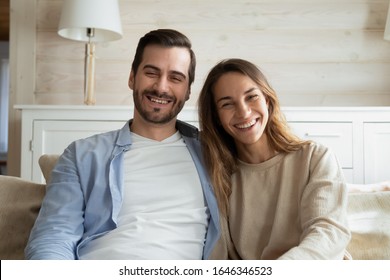 Happy Young Couple Sit On Couch In Living Room Look At Camera Talk On Video Call At Home, Smiling Millennial Man And Woman Having Webcam Conversation Using Unlimited Internet Connection