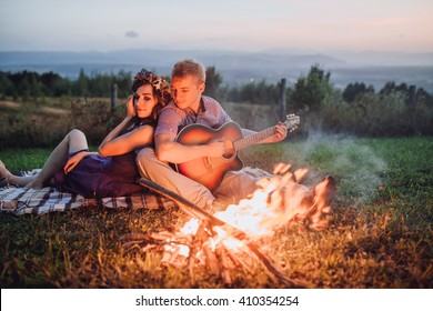 Happy young couple sitting by bonfire with guitar - Powered by Shutterstock