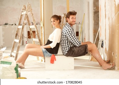 Happy Young Couple Sitting Happy In Home Under Construction.