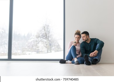 Happy Young Couple Sitting Near Window At Home On Cold Winter Day