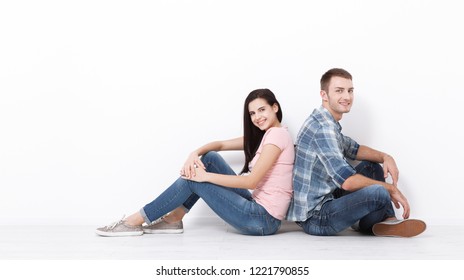 Happy young couple sitting on floor looking up while dreaming their new home and furnishing. Mock up for design.