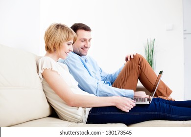 Happy Young Couple Sitting On Couch Using Laptop