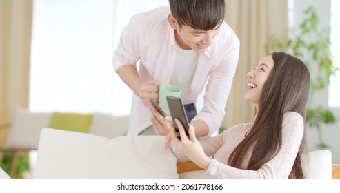 Happy Young Couple Sitting On  Couch And  Looking At Mobile Phone
