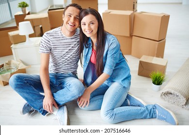 Happy young couple sitting on the floor of new house and looking at camera