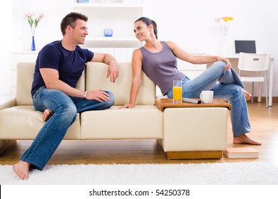 Happy Young Couple Sitting On Sofa At Home, Smiling.