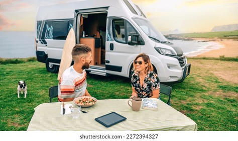 Happy young couple sitting outdoors in summer with camper van and beach on background - Powered by Shutterstock