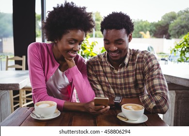 Happy young couple sitting at table using mobile phone in cafeteria - Shutterstock ID 458806294