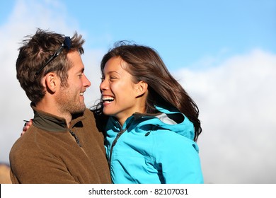 Happy Young Couple Smiling Outdoors Looking At Each Other With Love. Active Young Couple Portrait During Hiking Holidays. Asian Female Model And Caucasian Man Model.