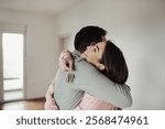 Happy young couple standing in hug and holding keys of new home, empty interior of apartment in background