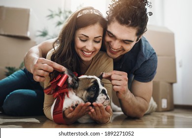 A happy young couple taking a break and having fun with their English bulldog puppy while moving into their new home. - Powered by Shutterstock