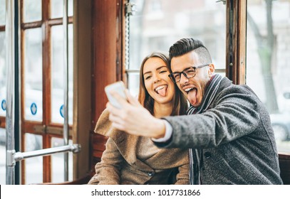 Happy young couple taking photos using mobile smart phone camera inside bus - Travel lovers making a self portrait to post on social media network - Relationship, love, smartphone addiction concept - Powered by Shutterstock