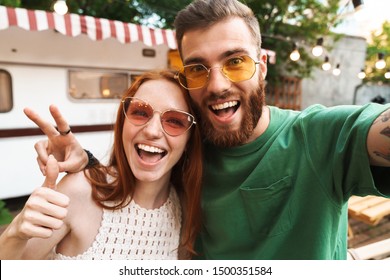 Happy young couple taking a selfie while standing outdoors with a trailer on a background, hugging - Powered by Shutterstock