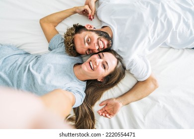 Happy young couple taking selfie portrait with smart mobile phone lying on bed - Two lovers moving in new home  - Powered by Shutterstock