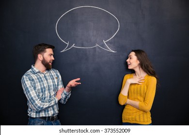 Happy young couple talking over chalkboard background with drawn empty dialogue - Shutterstock ID 373552009