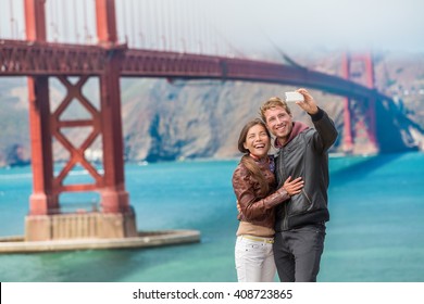 Happy young couple tourists taking selfie in San Francisco by Golden Gate Bridge, USA. Interracial young modern couple using smart phone. Asian woman, Caucasian man. - Powered by Shutterstock