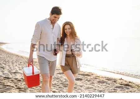 Happy young couple two friend family man woman in white clothes hold beer bottle bag refrigerator have picnic rest together at sunrise over sea beach ocean outdoor seaside in summer day sunset evening