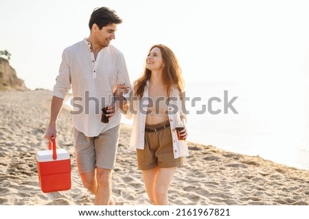Happy young couple two friend family man woman in white clothes drink beer hold bag refrigerator have picnic rest together at sunrise over sea beach ocean outdoor seaside in summer day sunset evening
