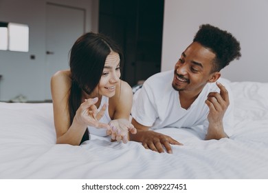 Happy young couple two man woman family in casual white clothes lying in bed on stomach communicate explain spend time together in bedroom lounge home house wake up dream be lost in reverie good day