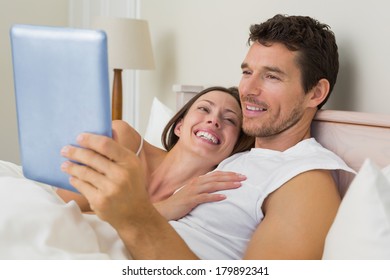 Schönes junges Ehepaar, das digitale Tablette zu Hause im Bett benutzt
