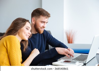 Happy Young Couple Using Laptop Computer At Home