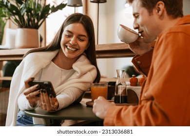 Happy young couple using mobile phone while sitting at table in cafe - Powered by Shutterstock