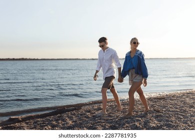 Happy young couple walking on the beach during sunset, prepairing for picnic. - Powered by Shutterstock