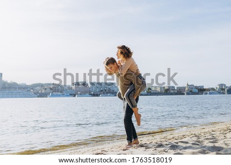 Happy young couple walking on the beach. Handsome guy carries a girl in his arms. Loving couple having fun they laugh hugging each other