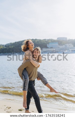 Happy young couple walking on the beach. Handsome guy carries a girl in his arms. Loving couple having fun they laugh hugging each other