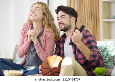 Happy Young Couple Watching Basketball Game On Tv At Home