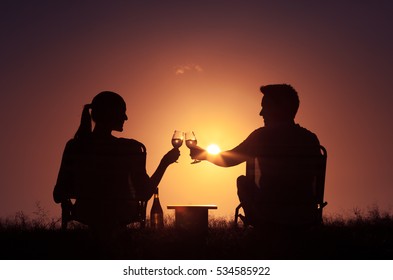 Happy young couple watching the sunset and enjoying a glass of wine. Relationship and friendship concept. 