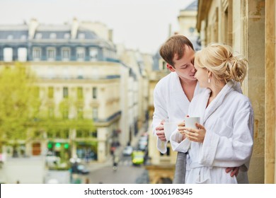 Happy young couple in white bathrobes drinking coffee together on balcony with view to Paris, France. Hotel, travel, relationships, and happiness concept - Powered by Shutterstock