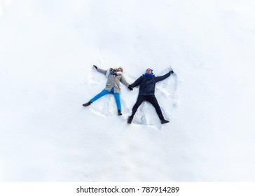 Happy Young Couple In Winter Park Lying On Snow. Making Snow Angel. Top View