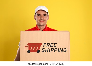 Happy Young Courier With Cardboard Box On Yellow Background. Free Shipping