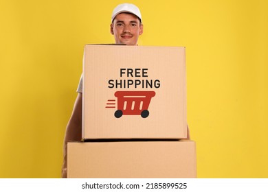 Happy Young Courier With Cardboard Boxes On Yellow Background. Free Shipping