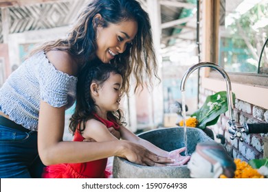 Happy Young Curly Asian Mother With Little Adorable Daughter Washing Hands In Sink Together Standing On Outside Terrace In Ethnic Style Smiling