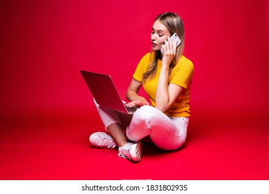 Happy Young Curly Beautiful Woman Sitting On The Floor With Crossed Legs And Using Laptop On Red Background.