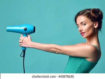 Happy young curly brunette woman with hair dryer on blue mint background. Hair style beauty concept