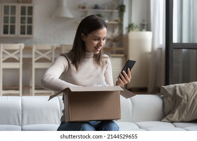 Happy young customer woman receiving purchase from internet store, using app on smartphone, giving feedback to shop, unpacking parcel from online shop, using cellphone, making delivery order