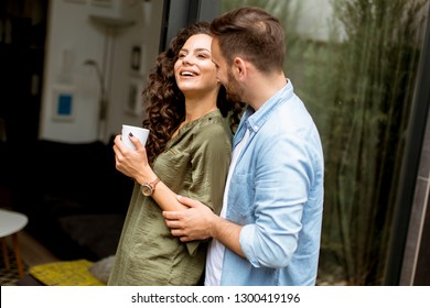 Happy young cute couple in love embracing each other and drinking coffee at home by the window - Powered by Shutterstock