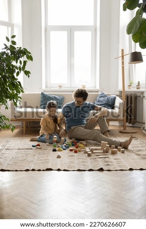 Happy young dad and preschooler kid girl playing on floor at home, constructing toy tower from wooden building blocks, training creative talent, imagination, enjoying leisure, learning game