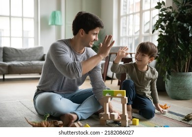 Happy young daddy giving high five to joyful small baby son, finishing constructing toy building with blocks. Bonding loving two male generations family involved in creative domestic activity. - Shutterstock ID 2182086027