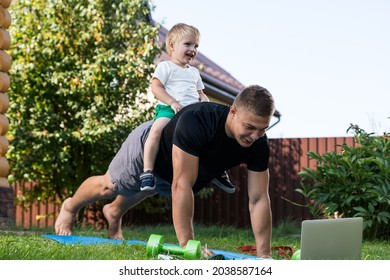 Happy Young Daddy Is Playing With  Her Baby  On A Green Lawn.Concept Of A Happy Family. Fathers Day. Dad And Son Have Activities Together On Holidays In Backyard 