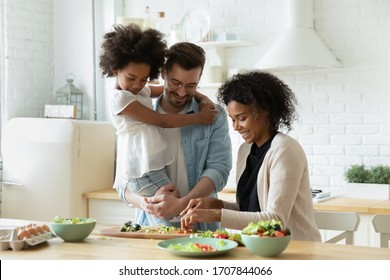 Happy Young Diverse Parents Have Fun Teach Little Biracial Daughter Cooking, Overjoyed Multiracial Family With Small Girl Child Preparing Food Making Healthy Salad For Breakfast In Kitchen Together